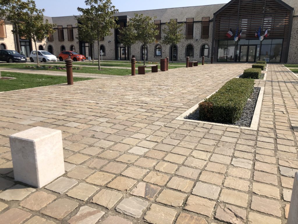 Photo d'une réalisation d'aménagement de sol sur la place de la mairie de Mignières dans le 28 en Eure et Loir, avec des pavés en grès neuf kandla de coloris ocre nuancé. Le pavage est en format 20x20 cm et offre un rendu soigné et durable, ce qui est adapté aux espaces publics.